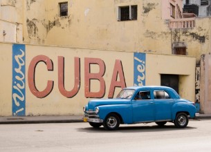 Picture of A vintage 1950s American car passing a Viva Cuba sign painted on a wall in cental Havana Cuba
