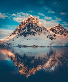 Picture of Antarctic landscape with snow covered mountains reflected in ocean water Sunset warm light on the mountain peak blue cloudy sky in the background Beautiful nature landscape Travel background