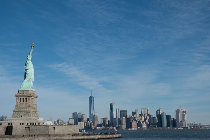 Picture of Statue of Liberty in Profile with Manhattan skyline in background Bright sunny day Wall Street and Financial District of lower Manhattan in the background  View from ferry across the harbor