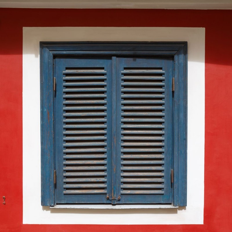 Afbeeldingen van A beautiful old window on a red wall with closed blue shutters The window is photographed in the old town in Riga