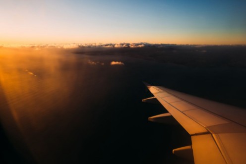 Afbeeldingen van View from airplane window above Portugal at sunset Sun shining from the corner of image on the aircraft wing with large water space beneath
