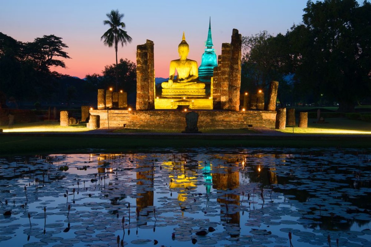 Afbeeldingen van Ancient sculpture of a sitting Buddha on the ruins of the temple of Wat Tra Phang Ngoen in the night illumination Sukhothai Park Thailand