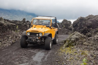 Bild på A curly-haired man is looking away driving an offroad yelow vehicle at the top of a valley with dark ground road