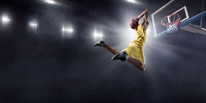 Basketball player makes slam dunk on big professional arena Player flies through the air with the ball Player wears unbranded clothes photowallpaper Scandiwall