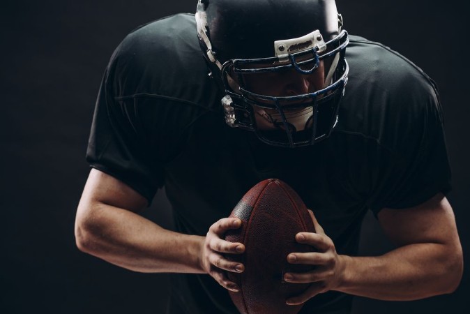 Picture of American football player with black helmet and armour running in motion holding ball getting ready to score a goal close up shot over dark background