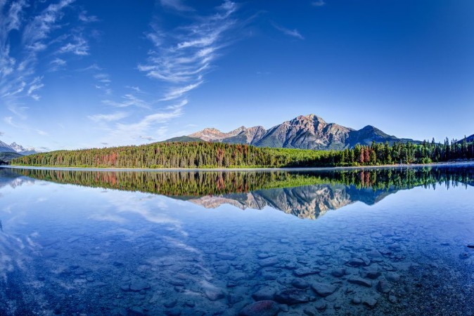 Afbeeldingen van Colorful trees lined the shores of Patricia Lake at Jasper National Park with Pyramid Mountain in the background The calm lake reflects a mirror image of the mountains and trees
