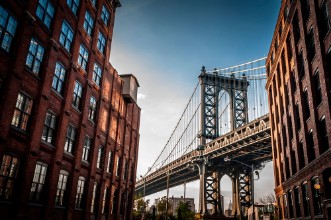 Picture of Manhattan bridge seen from a narrow alley enclosed by two brick buildings on a sunny day in summer