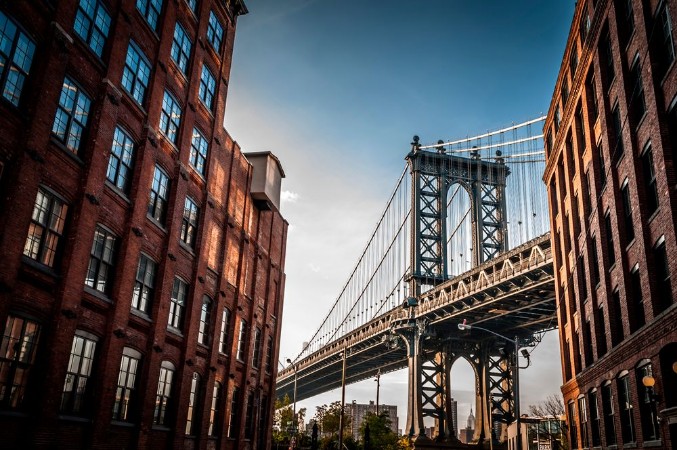 Afbeeldingen van Manhattan bridge seen from a narrow alley enclosed by two brick buildings on a sunny day in summer